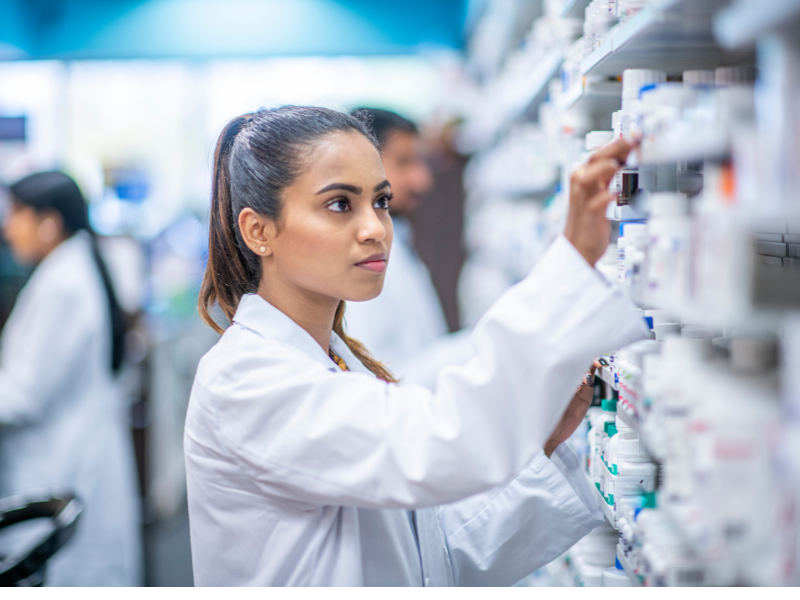 All'interno di una farmacia, una famacista vestita con il camice bianco prende un medicinale dallo scaffale dedicato